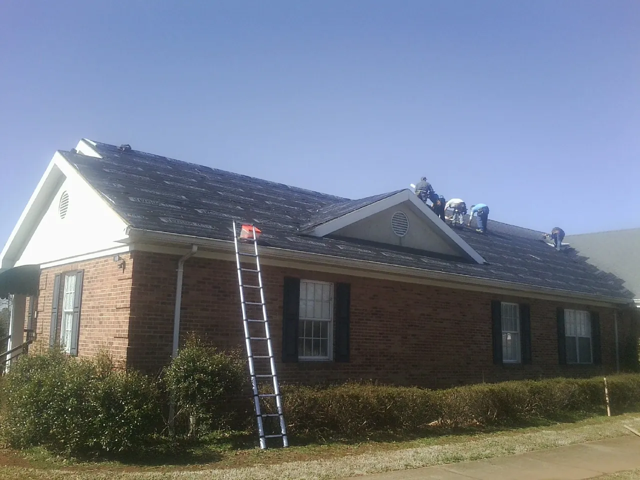 Crew tearing shingles off a brick ranch roof with a ladder set — Emergency Roof Repair work by our crew in Ravenna