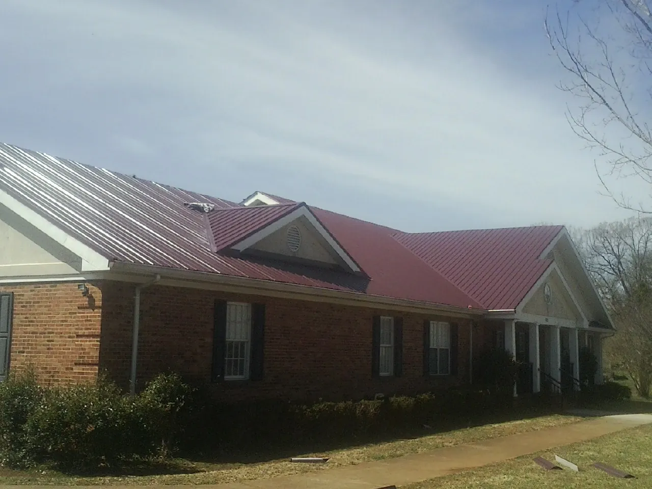 Red metal roof with gabled entries on a long brick building, from a Hail Damage Roof Repair job in Ravenna
