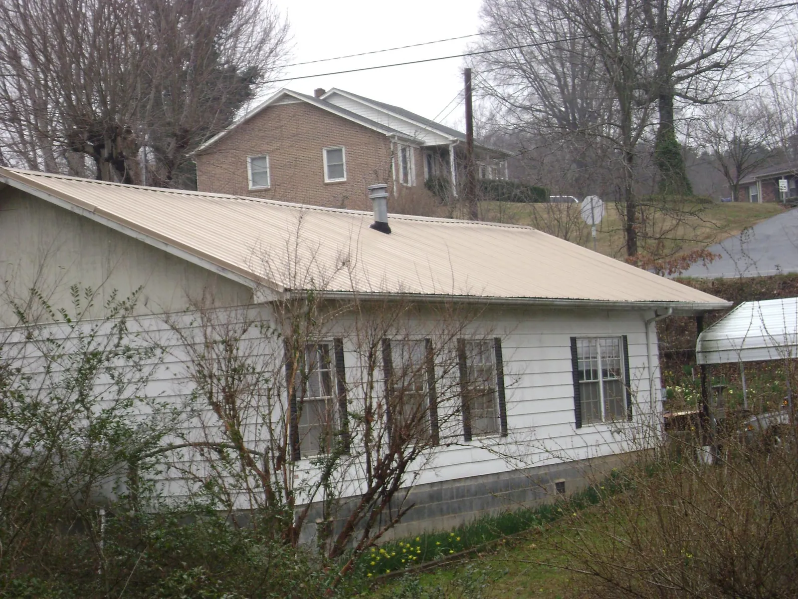 Tan metal roof on a white sided house set into a hillside — Commercial Roofing by Roofing Brothers in Ravenna